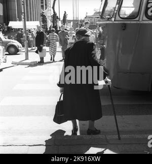 Senior en 1950s. Une dame âgée essaie de traverser la rue et attend un bus pour passer, elle garde son équilibre avec une canne. En arrière-plan Hötorget Stockholm Suède 1959. Kristoffersson réf. CH22-8 Banque D'Images