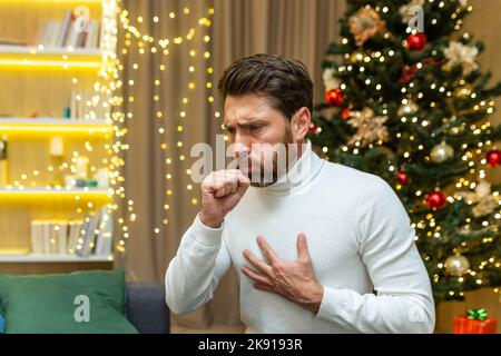 un homme tousse à noël à la maison assis seul sur un canapé malade les vacances du nouvel an dans le salon. Banque D'Images