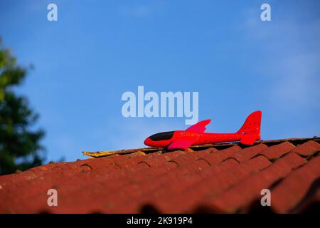 Un jouet d'avion de planeur en mousse rouge a atterri sur un toit contre un ciel bleu Banque D'Images