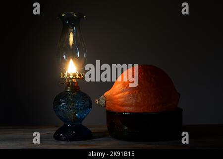 Une citrouille Hokkaido orange vif dans un bol en céramique et une lampe à huile brûlante Banque D'Images