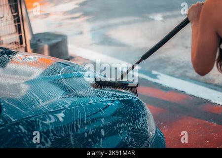 Un gros plan de la fille lavant une voiture avec une brosse dans le lavage automatique. Banque D'Images