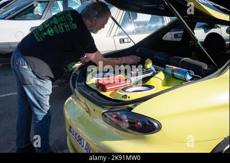 Un homme qui travaille sur un coupé Hyundai jaune réglé avec une chaîne stéréo et des jouets dans le coffre Banque D'Images