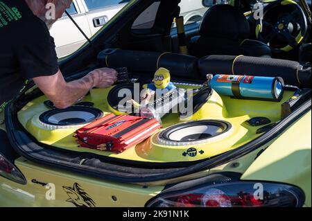 Un homme qui travaille sur un coupé Hyundai jaune réglé avec une chaîne stéréo et des jouets dans le coffre Banque D'Images