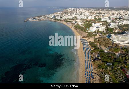 Vue aérienne du littoral avec plage organisée, Ayia Napa, Chypre. Paysage de drone de la côte de sable doré avec chaises longues et parasols Banque D'Images