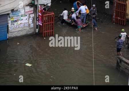 Les propriétaires de pousse-pousse ont du mal à traverser une rue engortée à la suite de fortes pluies qui causent beaucoup de souffrances aux piétons et aux navetteurs. Le cyclone Sitrang frappe le Bangladesh en train d'établir des liaisons de communication et d'alimentation, inondant les rues pour faire encore des activités. Banque D'Images