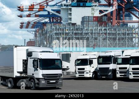 Camions dans le port maritime international contre un fond de navire chargé de conteneurs. Concept de commerce international et de logistique Banque D'Images