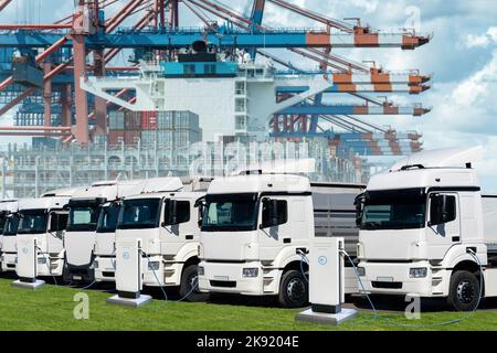 Camions électriques dans le port maritime international contre un fond de navire chargé de conteneurs. Banque D'Images