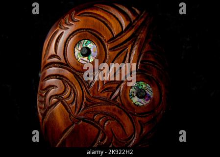 Hei Tiki en bois maori sculpté à la main avec des yeux de coquillages de paua. Taonga de Nouvelle-Zélande. Gros plan arrière-plan sombre. Banque D'Images