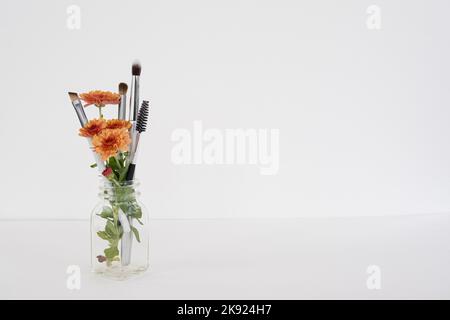 Décor minimaliste avec fleurs orange et quatre pinceaux de maquillage. Banque D'Images