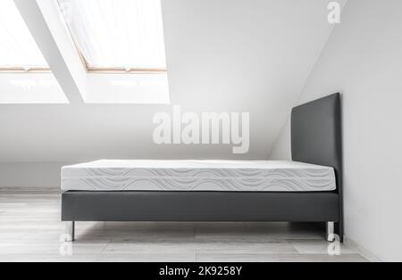 Nouveau lit double dans une chambre moderne et peinte dans une salle d'eau blanche lumineuse avec deux fenêtres sur le toit. Mobilier de maison après avoir été déplacé. Banque D'Images