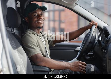 Vue latérale d'un liveur souriant conduisant un camion et regardant la caméra Banque D'Images