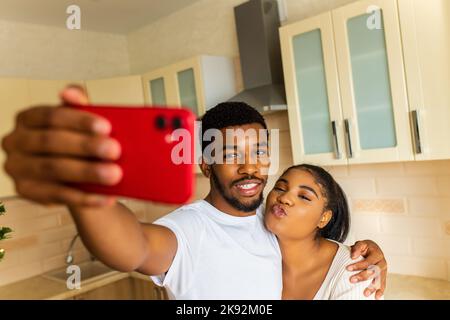 Couple multiethnique joyeux prenant un selfie à la cuisine Banque D'Images