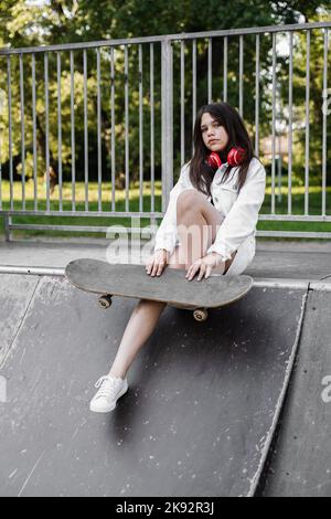 Enfant patineur avec planche à roulettes et casque assis sur une rampe de sport. Style de vie sport extrême. Publicité créative pour le magasin de sport pour enfants Banque D'Images
