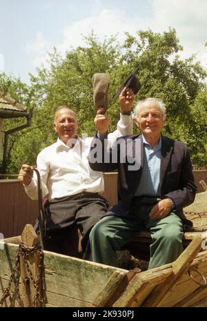 Comté de Covasna, Roumanie, environ 2002. Des hommes qui font monter un chariot tiré par des chevaux et qui agite leurs chapeaux pour Gesture Au revoir. Banque D'Images