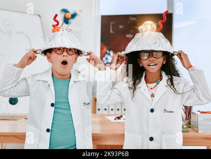 Le professeur a déclaré que nous devrions mettre nos chapeaux de réflexion sur : deux adorables jeunes élèves qui font une expérience de l'électricité et de la lumière en classe scientifique Banque D'Images