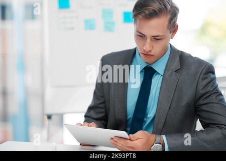 Rester à la pointe de la technologie. Un beau jeune homme d'affaires assis seul dans son bureau et utilisant une tablette. Banque D'Images