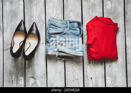 short en denim avec veste rouge et chaussures en cuir noir sur une table en bois blanc, vêtements pour femmes sur la table Banque D'Images