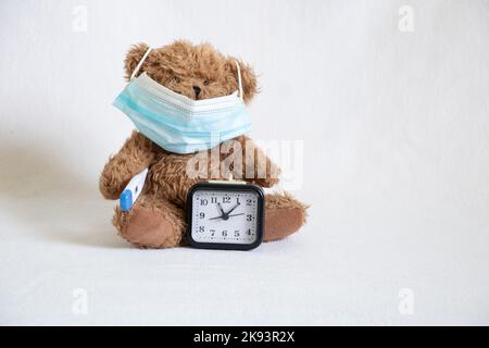 ours en peluche brun dans un masque médical avec un thermomètre et une montre est debout à proximité, la morbidité infantile, la maladie et la santé Banque D'Images