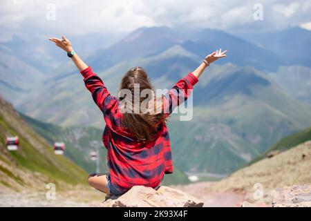 Une heureuse femme touriste sur le sommet de la montagne a levé les mains, jouit de la vue magnifique sur les montagnes. Banque D'Images