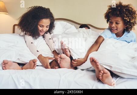 C'est la façon dont nous réveillons maman et papa. Deux adorables petits enfants chatouillent les pieds de leurs parents tout en se relaxant au lit ensemble à la maison. Banque D'Images
