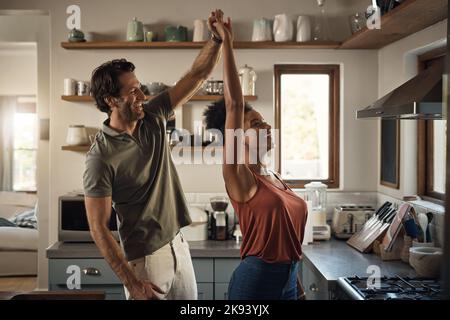 Il aime danser avec sa reine. Un jeune couple affectueux dansant ensemble dans leur cuisine à la maison. Banque D'Images