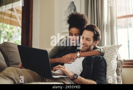 Nous aimons toujours passer du temps ensemble à l'intérieur. Un jeune couple heureux utilisant un ordinateur portable tout en se relaxant sur un canapé dans leur salon à la maison. Banque D'Images