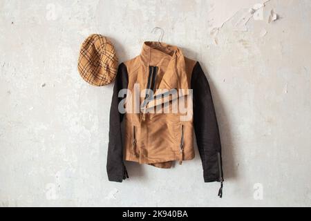 une veste marron pour femmes et une casquette à carreaux sont accrochées sur un mur blanc à la maison Banque D'Images