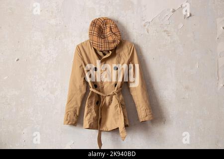 imperméable marron élégant pour femme et casquette à carreaux accrochés sur un mur blanc à la maison Banque D'Images