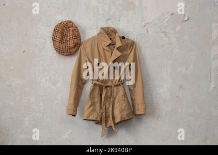 imperméable marron élégant pour femme et casquette à carreaux accrochés sur un mur blanc à la maison Banque D'Images