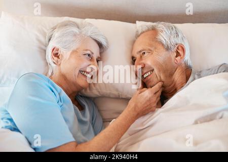 Vous me faites toujours si heureux. Un couple affectueux et senior se regardant les uns les autres avec amour tout en étant allongé dans leur maison de repos. Banque D'Images