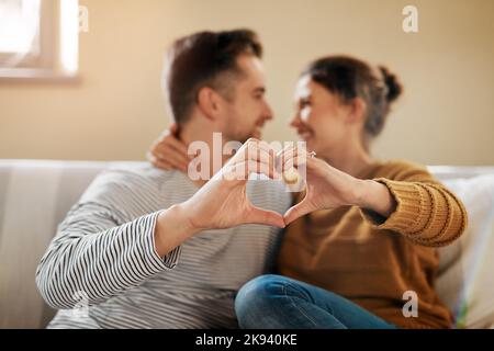 L'amour vit ici. Un couple formant un coeur avec leurs mains tout en étant assis ensemble. Banque D'Images