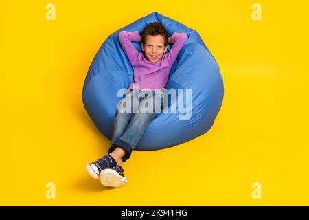 Portrait en longueur d'une personne joyeuse et paisible assise sac confortable mains derrière la tête isolé sur fond jaune Banque D'Images