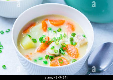 Soupe de poisson à la morue avec pois verts, pommes de terre et carottes dans un bol blanc. Banque D'Images