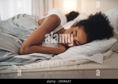 Je déteste aller me coucher se sentant ainsi. Une jeune femme a l'air bouleversée en étant au lit avec son partenaire. Banque D'Images