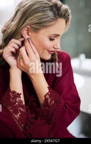 Ces boucles d'oreilles me font déjà sentir belle. Une belle jeune mariée mettant sur ses boucles d'oreilles tout en préparant son mariage dans son dressing. Banque D'Images