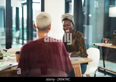 Le partage d'idées est essentiel à la réussite. Une jeune femme d'affaires attirante qui s'assoit et rit avec sa collègue féminine au bureau. Banque D'Images
