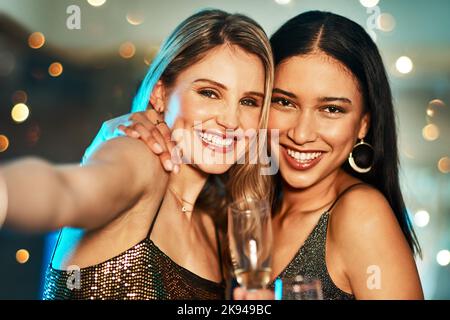 Toujours une explosion avec vous. Portrait de deux jeunes femmes gaies prenant un autoportrait ensemble à l'intérieur d'un bar la nuit. Banque D'Images