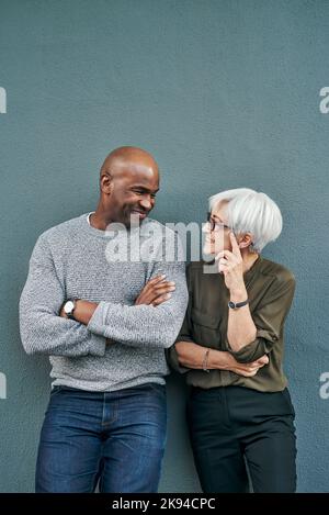 Nous avons eu la même chose à l'esprit : deux hommes d'affaires joyeux et mûrs qui ont une discussion tout en se tenant contre un mur à l'extérieur. Banque D'Images