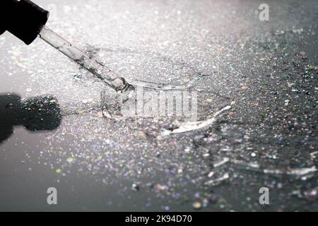 Dégradé. Rétroéclairage. Pipeter avec du sérum ou du gel sur fond noir avec paillettes. Acide hyaluronique hydratant. Gel antibactérien. Cosmétologie. Eau. Banque D'Images