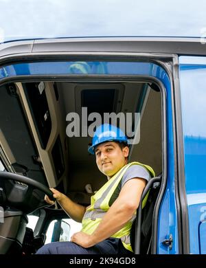 Un conducteur caucasien portant un casque et un gilet de sécurité et assis sur le siège conducteur du camion Banque D'Images