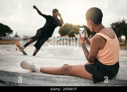 Homme sur le skateboard dans le parc, femme photographie le petit ami du patineur en ville sur un smartphone ou un mode de vie urbain à Los Angeles. Mode de rue, jeune noir tendance Banque D'Images