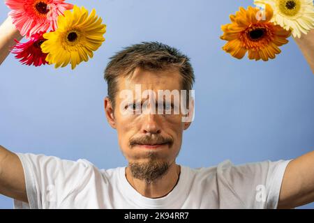 Un homme en colère et irrité dans un T-shirt blanc secoue et balance des fleurs Banque D'Images