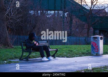 Un homme dans une casquette est assis sur un banc le jour d'hiver à Gladstone Park, Londres, Angleterre Banque D'Images