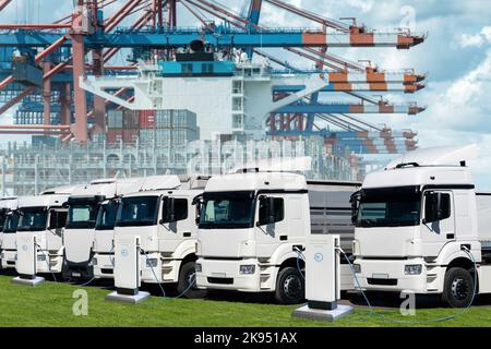 Camions électriques dans le port maritime international contre un fond de navire chargé de conteneurs. Banque D'Images