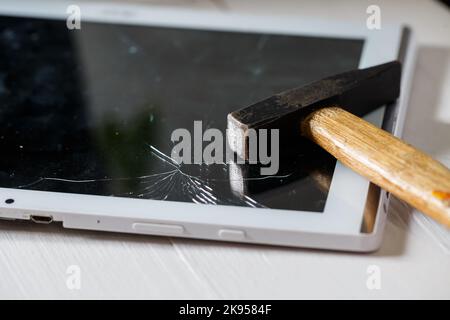 Le marteau frappe la tablette tactile cassée, ce qui suggère qu'il est sur le point de la remplacer. Réparation de tablette de verre cassée Banque D'Images