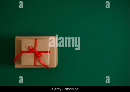 Une vue de dessus des paquets cadeaux beige avec ruban rouge en forme d'arc sur une surface verte de forêt Banque D'Images