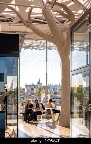 Voyageurs ayant une pause dans le hall de la gare SNCF de Nantes, France, conçu par Rudy Ricciotti, avec le château de Nantes au loin. Banque D'Images