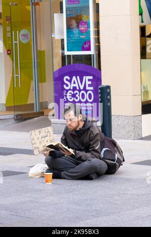 Irlande Dublin Grafton Street Beggar lecture livre sans-abri homme jeune signe - si j'ai €2 euros de 10 personnes je vais obtenir un repas chaud et un lit ce soir Banque D'Images