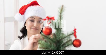 Bannière souriante latine ou femme d'affaires indienne décorant l'arbre de noël dans l'espace de copie de bureau. Bonne femme du Moyen-Orient décorant l'arbre pour noël Banque D'Images