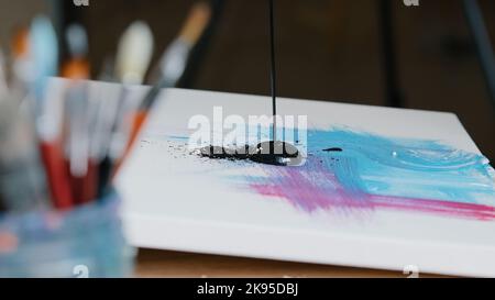 Gros plan noir foncé taches de peinture sur la toile avec rose et bleu image femelle main tenant la main pinceaux de peinture dessine la texture crée Banque D'Images